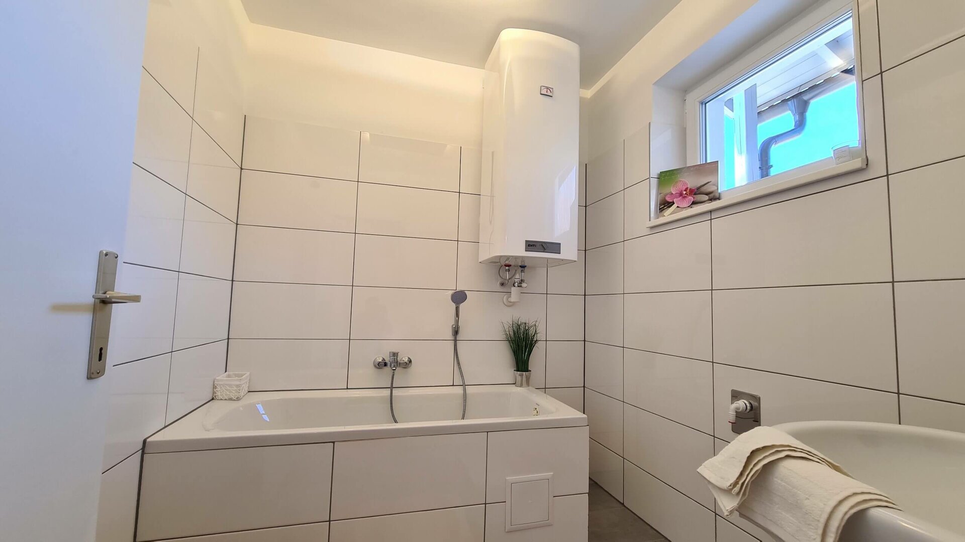 Weißes Badezimmer mit Badewanne und kleinen Dekoelementen